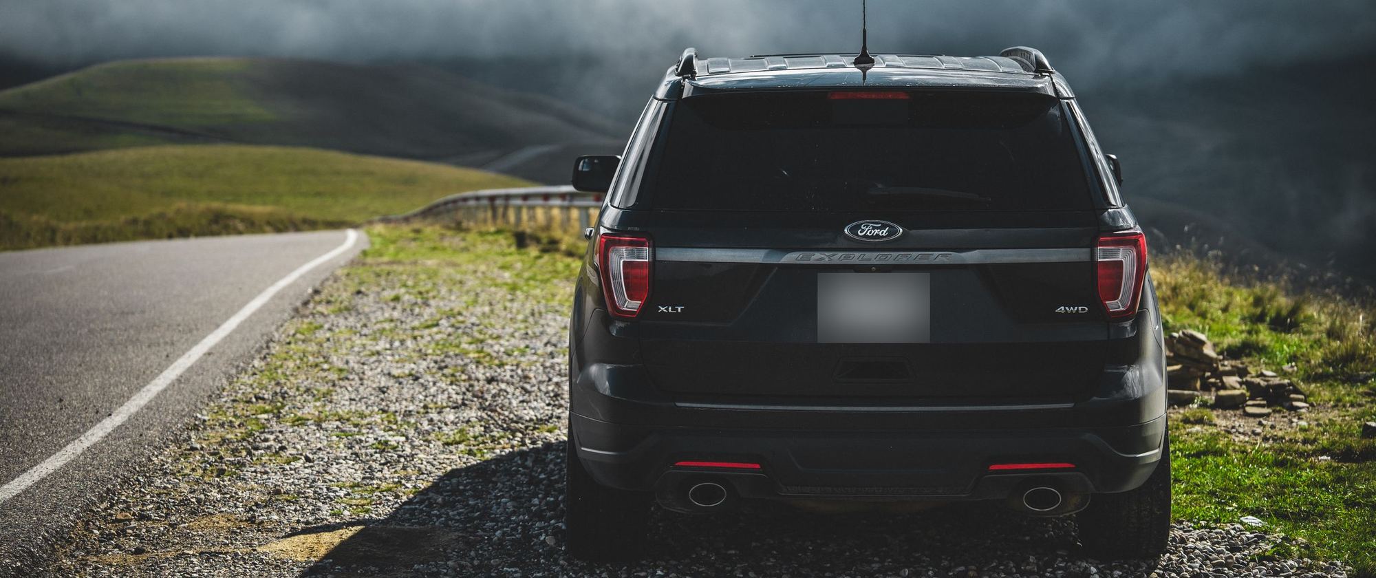 Rear view of a black Ford Explorer parked on a gravel roadside